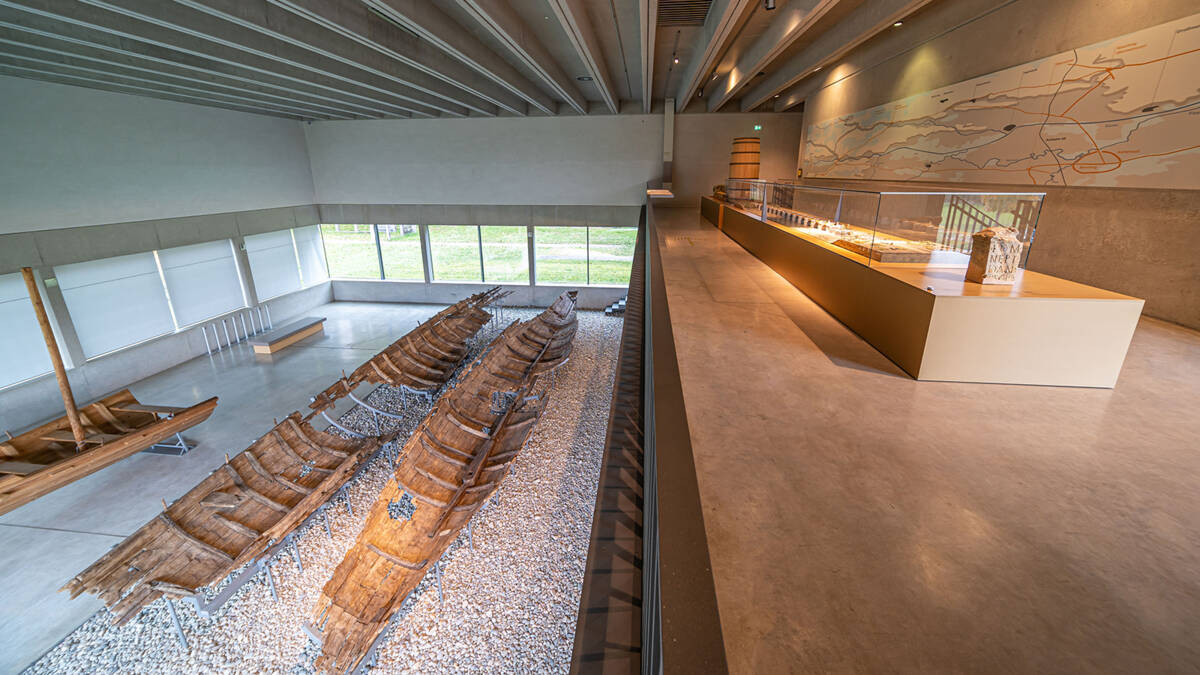 Links die Bootswracks von Oberstimm in der Schiffshalle des Museums, rechts Brückenmodell, Karte und Objekte zur römischen Infrastruktur an der Donau.